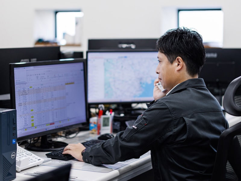 PCを見ながら電話で取引先とやり取りするタツミトランスポートのスタッフ