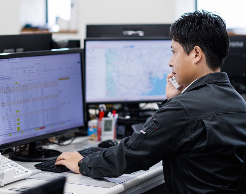 PCを見ながら電話で取引先とやり取りするタツミトランスポートのスタッフ